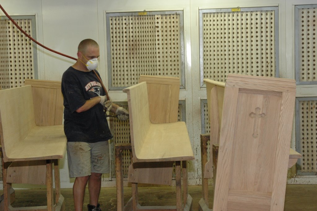 worker refinishing a wooden church pew in shop